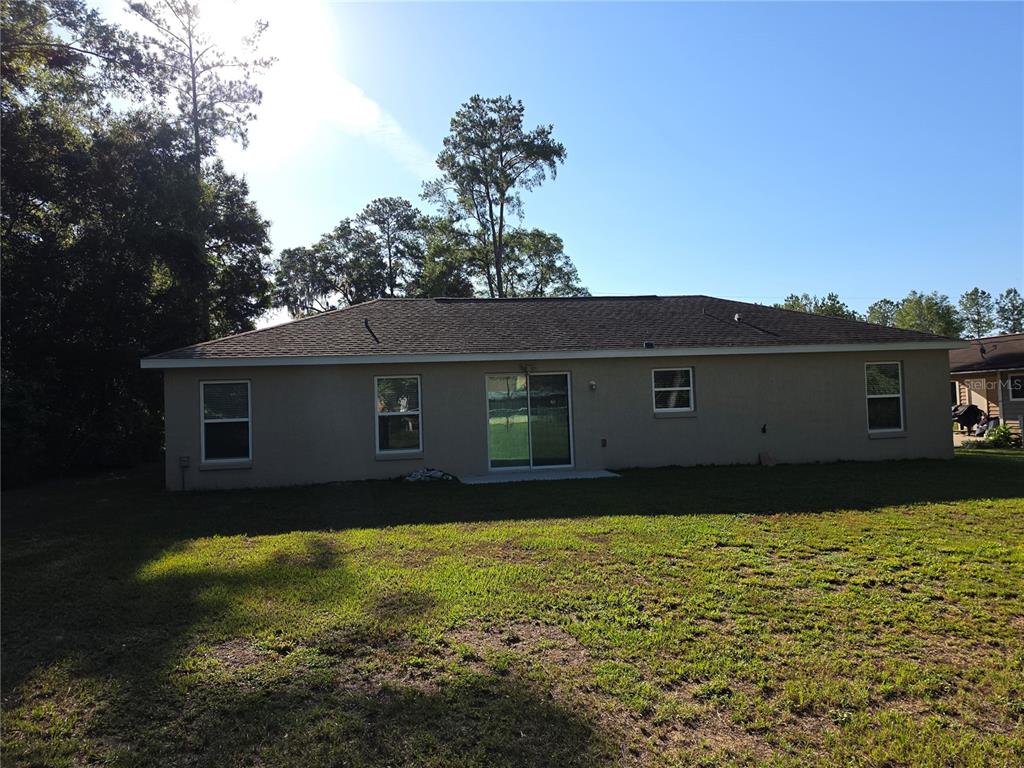 The exterior rear view of a single-story house features a tan stucco facade and lawn — 5436 NW 60TH TERRACE, OCALA, FL