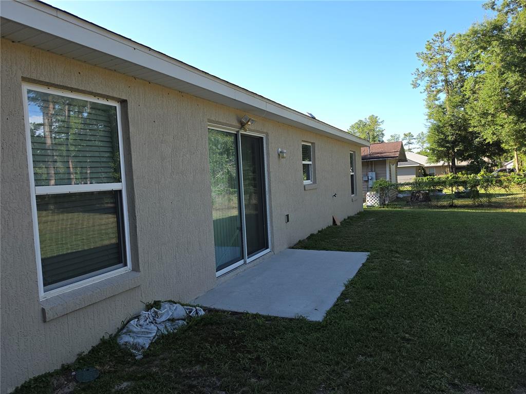 The exterior of a beige stucco house features a sliding glass door and concrete patio — 5436 NW 60TH TERRACE, OCALA, FL