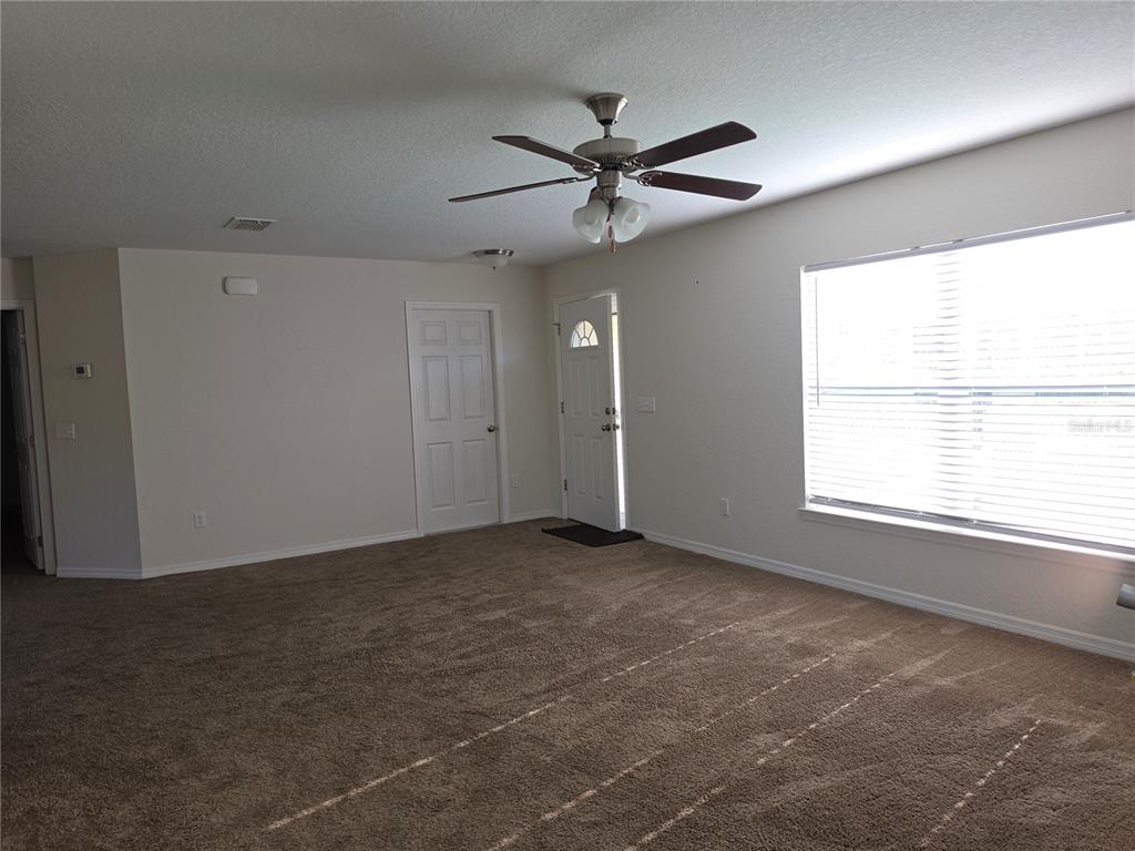 An empty living room features beige carpet, a ceiling fan, and a white entry door — 5436 NW 60TH TERRACE, OCALA, FL