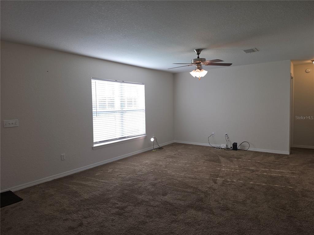 An empty room features beige walls, brown carpeting, a ceiling fan, and a single window — 5436 NW 60TH TERRACE, OCALA, FL