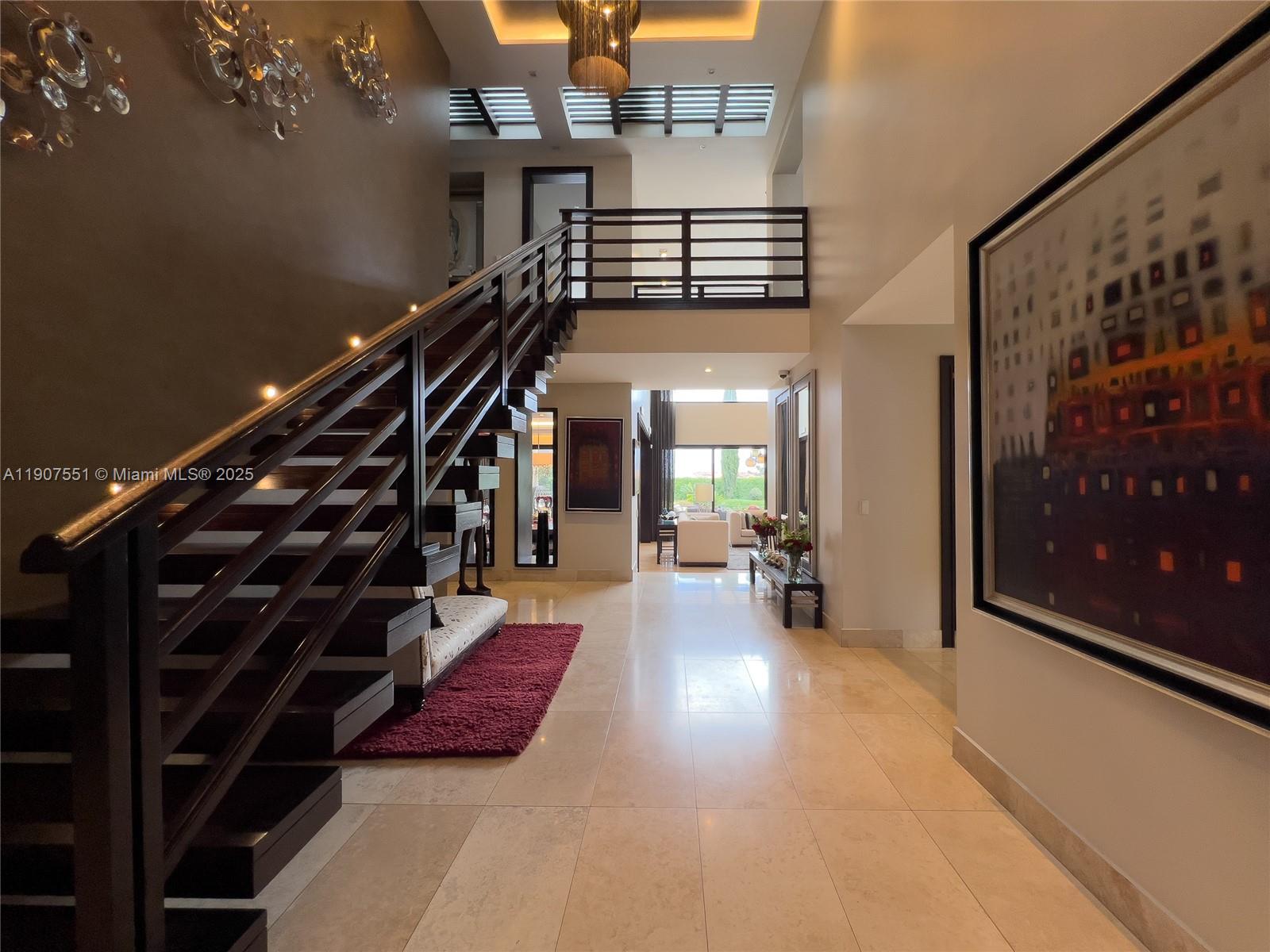 A grand foyer features a dark wood staircase, tile flooring, and a large wall painting — Rincon Del Valle Cumbaya Quito, EC, EC