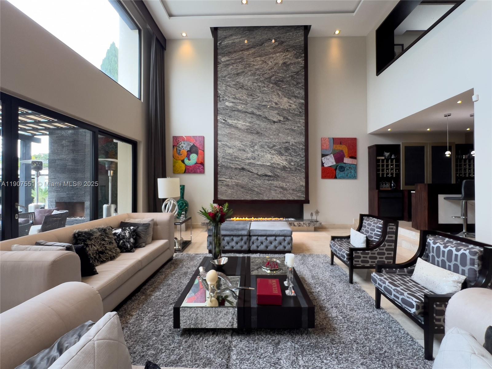 A high-ceilinged living room features a large stone fireplace, modern furniture, and floor-to-ceiling windows — Rincon Del Valle Cumbaya Quito, EC, EC