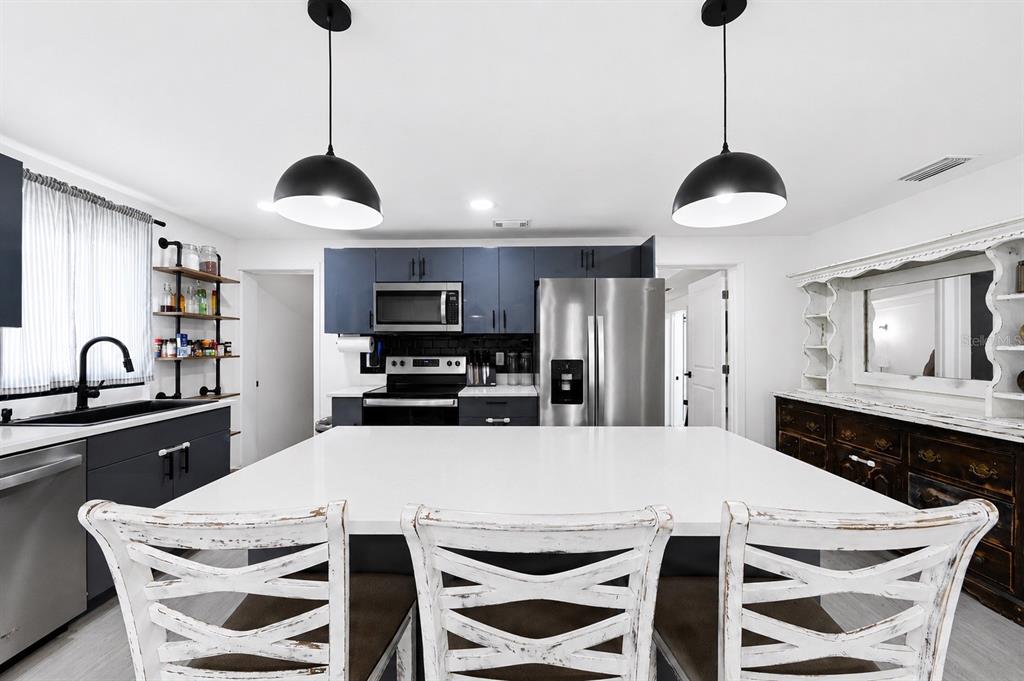 A kitchen features a large white island, dark blue cabinets, stainless steel appliances, and pendant lighting — 4114 W OLIVE STREET, TAMPA, FL