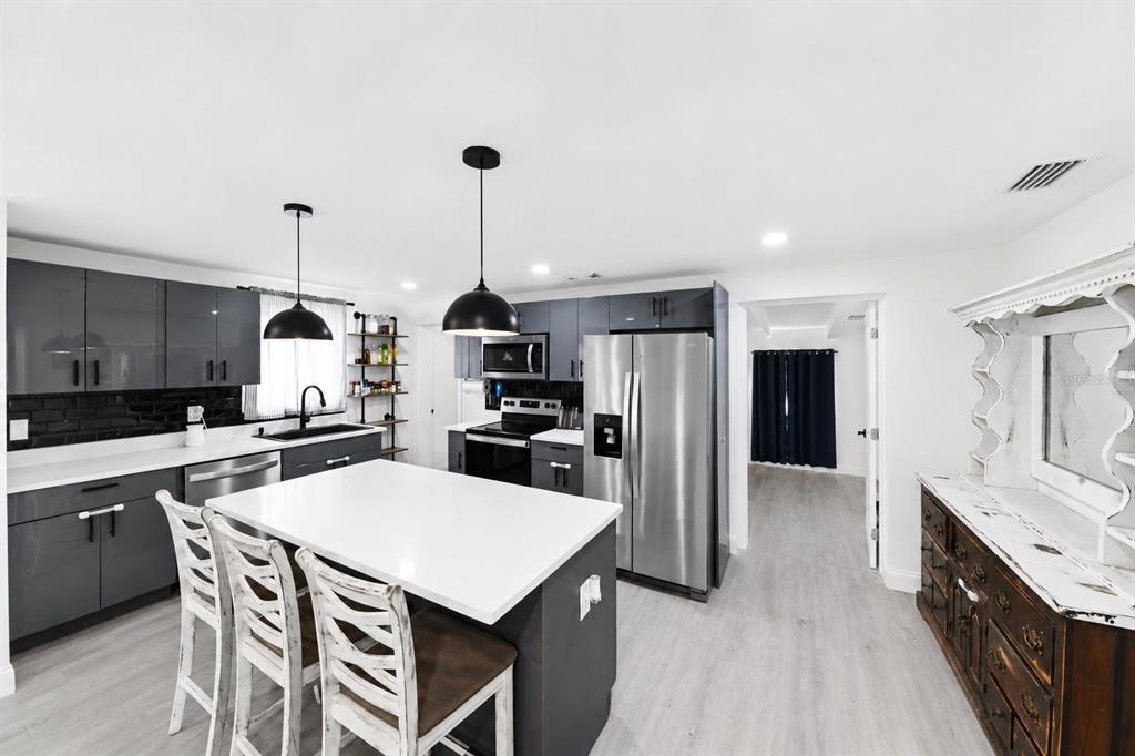 A modern kitchen features gray cabinets, a white island with seating, and stainless steel appliances — 4114 W OLIVE STREET, TAMPA, FL