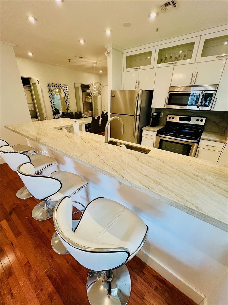 A kitchen features a stone breakfast bar, white cabinetry, stainless steel appliances, and wood flooring — 600 Euclid Ave # 5B, Miami Beach FL 33139, MIAMI BEACH, FL