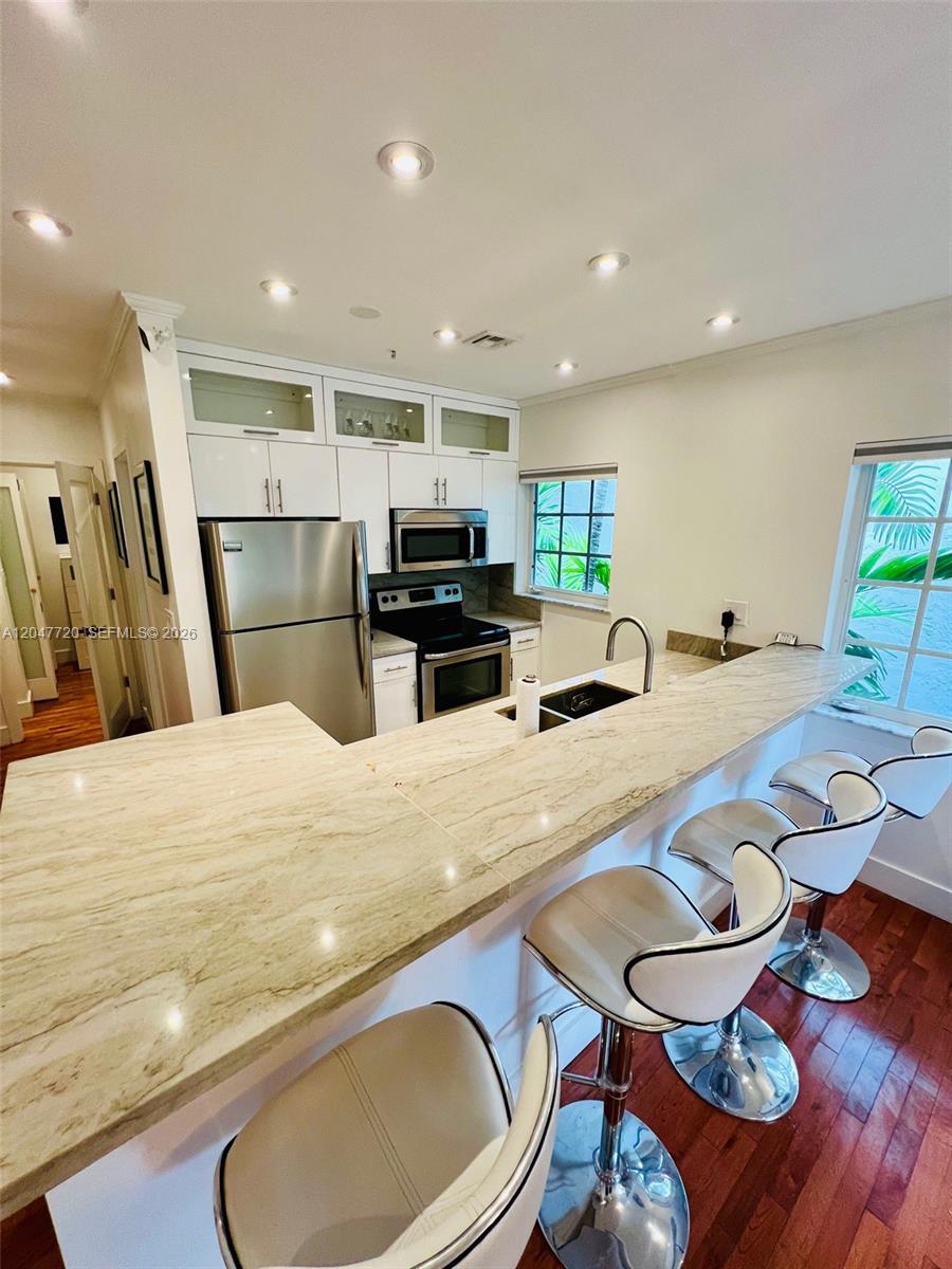 A kitchen features white cabinets, stainless steel appliances, and a stone breakfast bar with stools — 600 Euclid Ave # 5B, Miami Beach FL 33139, MIAMI BEACH, FL
