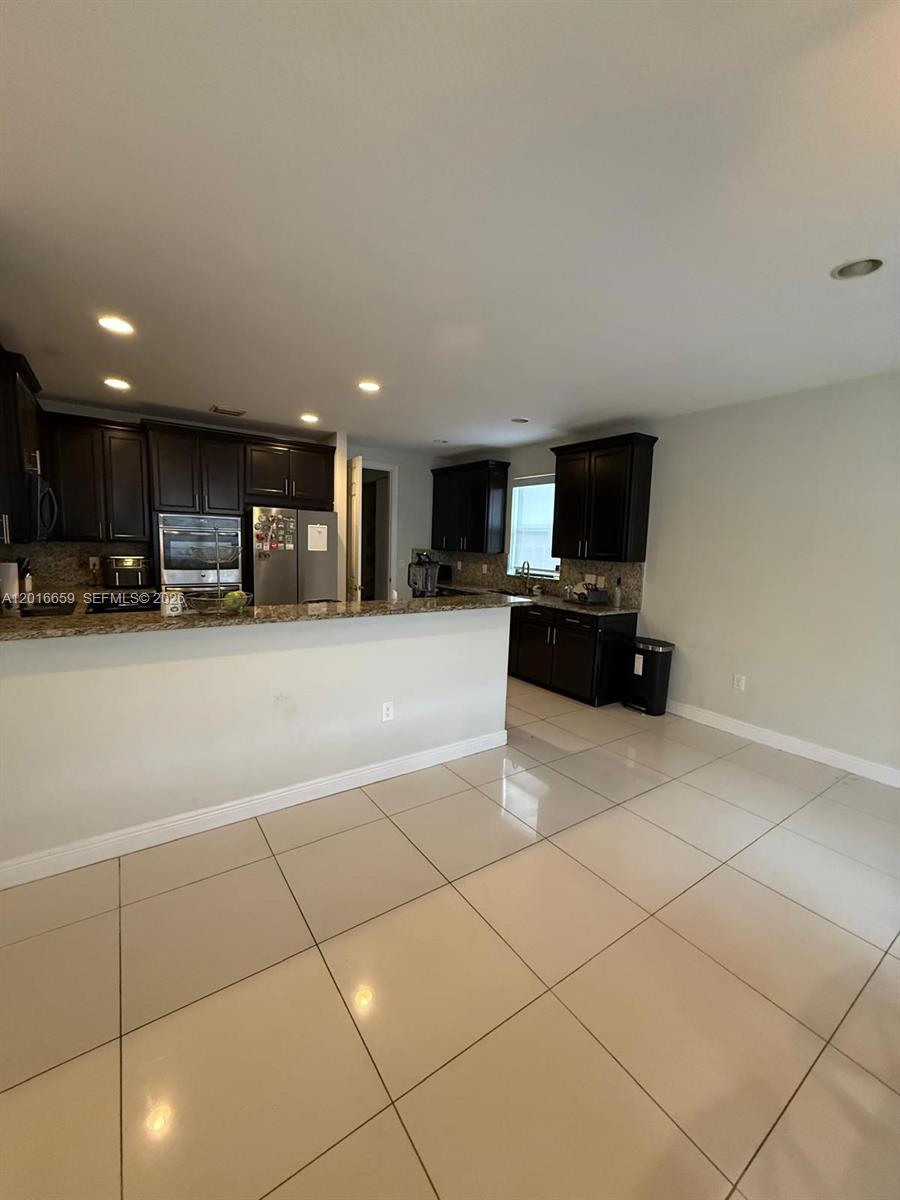 A kitchen features dark wood cabinets, granite countertops, and light-colored tile flooring — 9845 NW 86th Ter, Doral FL 33178, DORAL, FL