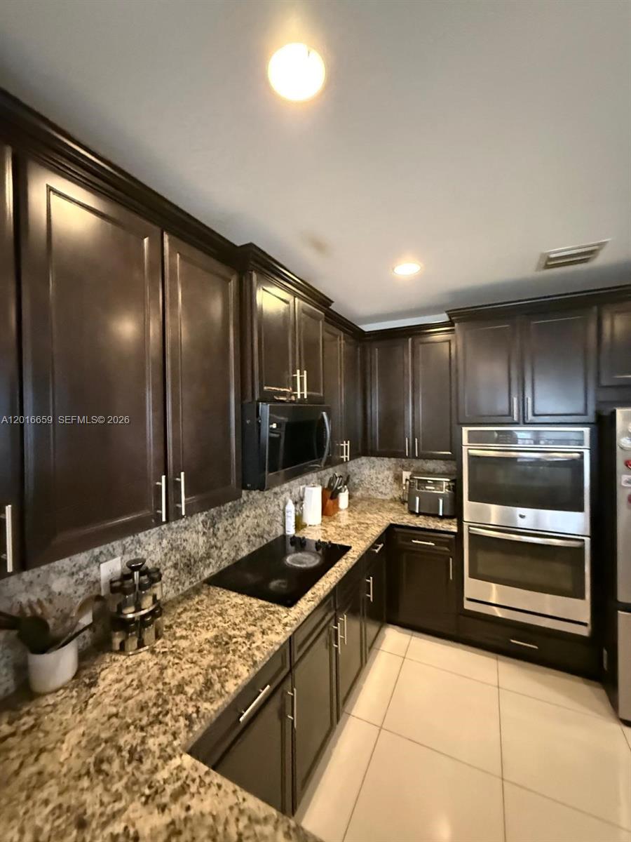 A kitchen features dark wood cabinets, granite countertops, and stainless steel double wall ovens — 9845 NW 86th Ter, Doral FL 33178, DORAL, FL