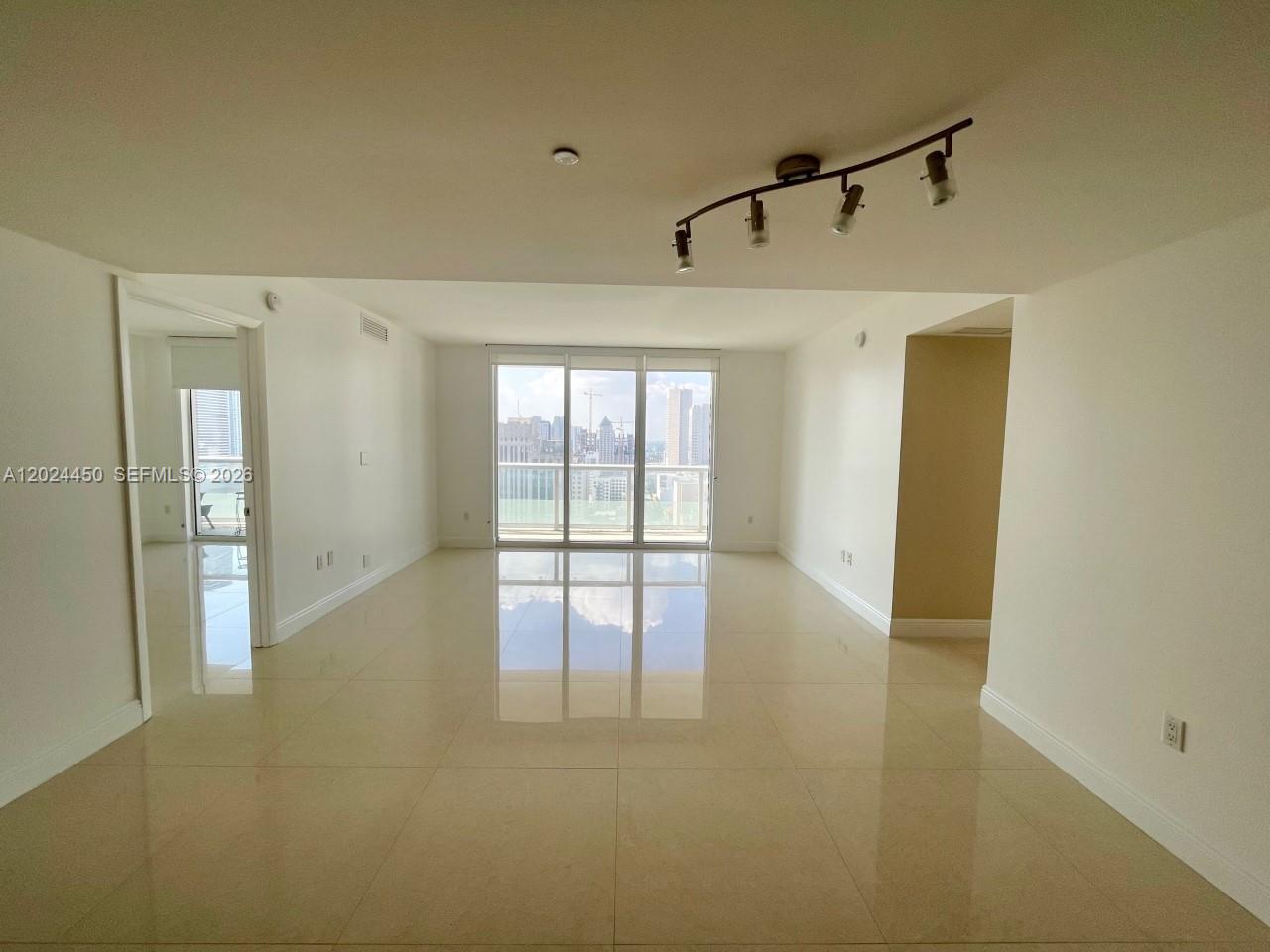 An empty living room features polished tile floors, recessed lighting, and a balcony with city views — 50 Biscayne Blvd # 2401, Miami FL 33132, MIAMI, FL