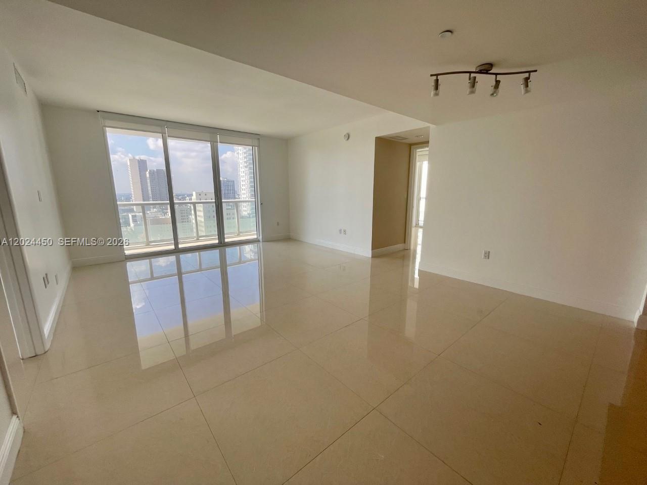 An empty living room features large windows, light-colored tile flooring, and a modern ceiling light — 50 Biscayne Blvd # 2401, Miami FL 33132, MIAMI, FL