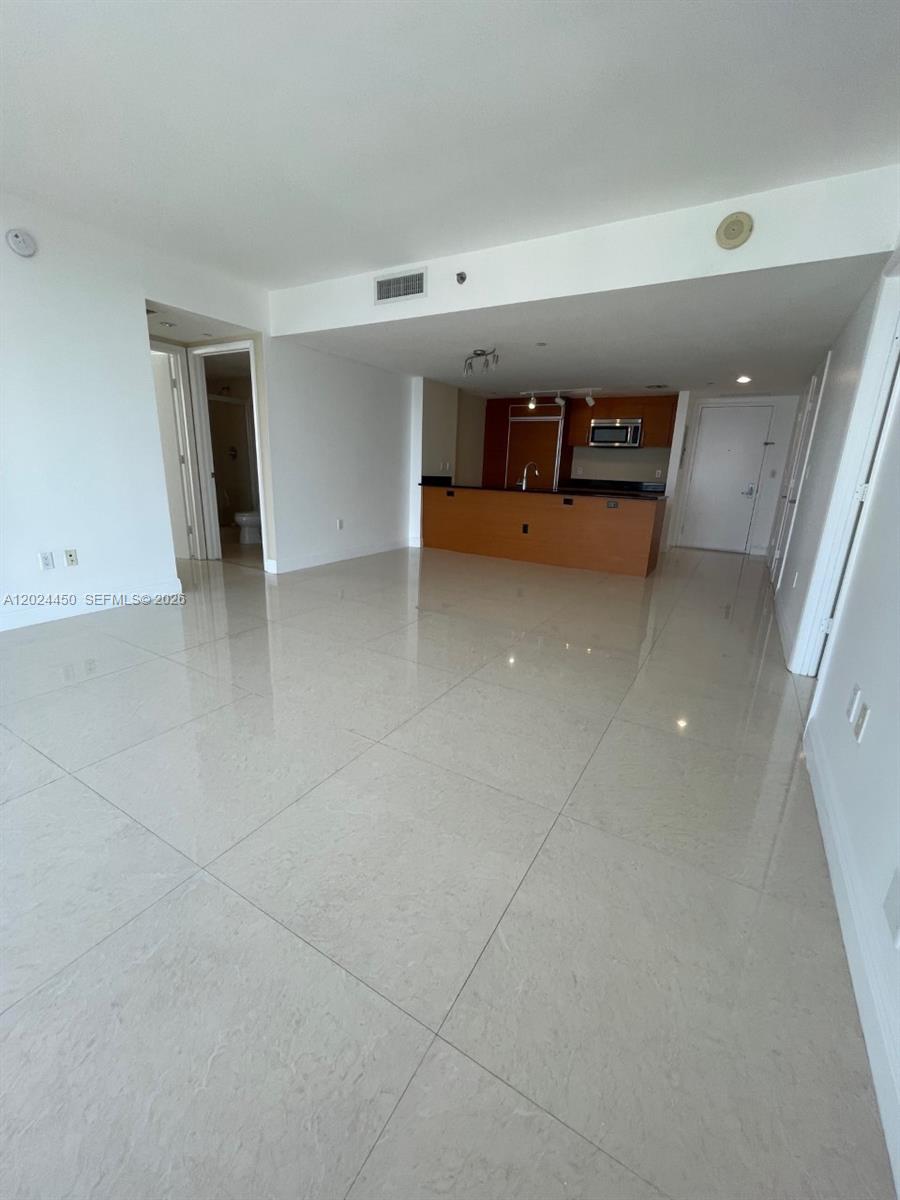 An open-concept living area features light-colored tile flooring and a kitchen with wood cabinetry — 50 Biscayne Blvd # 2401, Miami FL 33132, MIAMI, FL