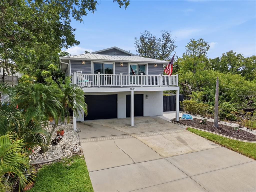 A two-story elevated house features a white balcony, gray siding, and a concrete driveway — 2811 AVENUE C, HOLMES BEACH, FL