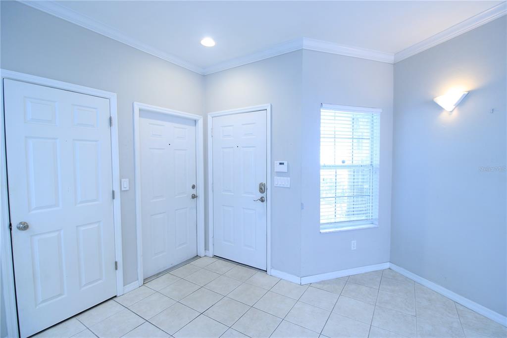 An entryway features light-colored tile flooring, three white doors, and a window with blinds — 4742 NW 79TH ROAD, GAINESVILLE, FL