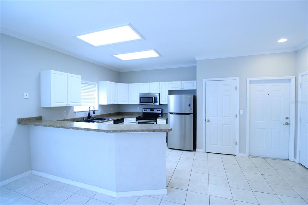 A kitchen with white cabinets, stainless steel appliances, and a breakfast bar on tiled floors — 4742 NW 79TH ROAD, GAINESVILLE, FL