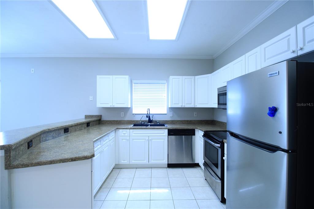 A kitchen features white cabinets, stainless steel appliances, and a granite countertop breakfast bar — 4742 NW 79TH ROAD, GAINESVILLE, FL