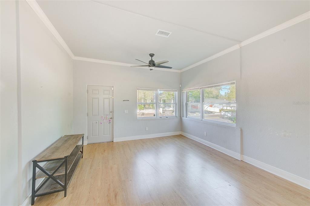 An empty living room features light wood-look flooring, white walls, a ceiling fan, and windows — 2905 E 21ST AVENUE, TAMPA, FL