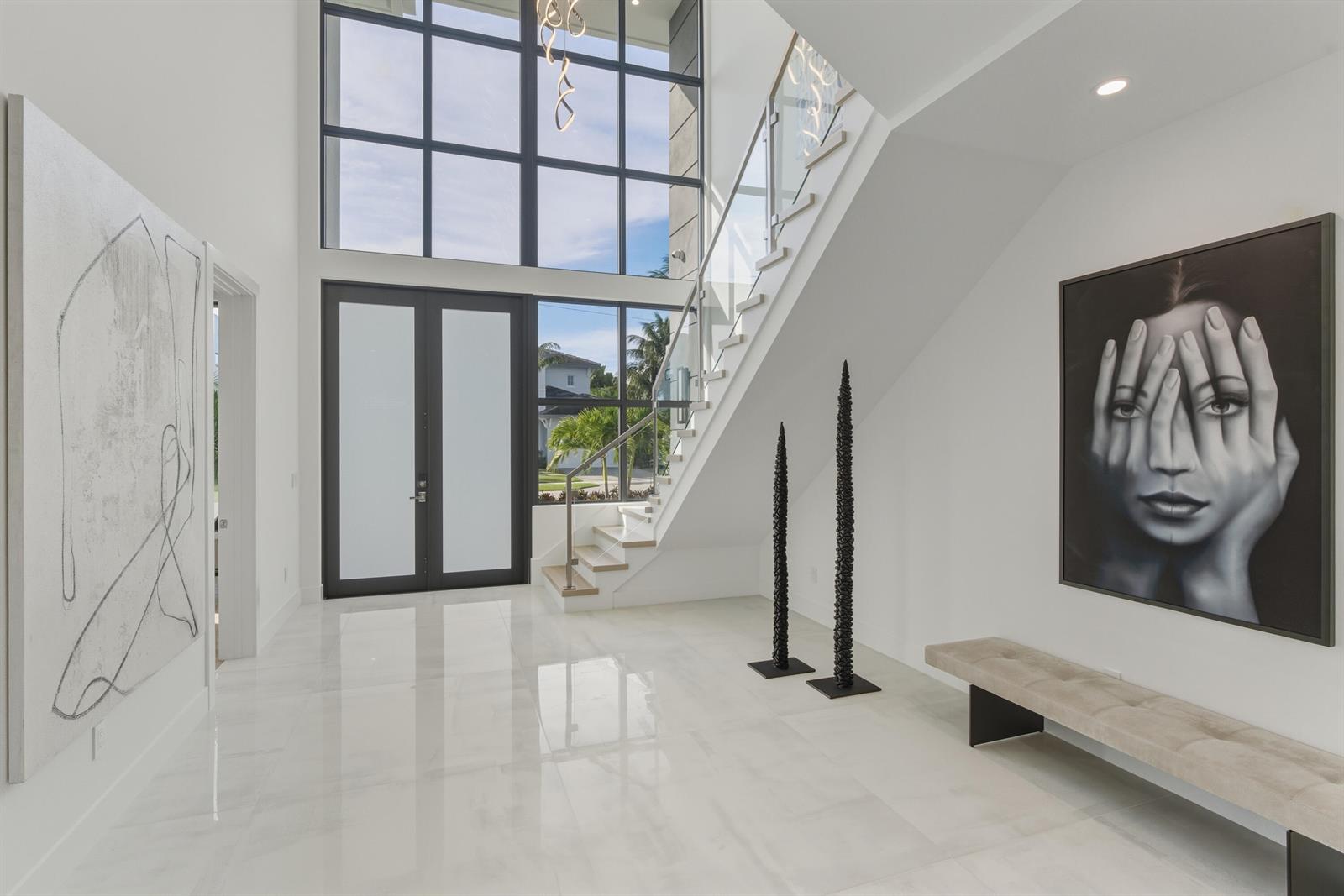 A bright, modern foyer features white tile floors, a glass-railed staircase, and large windows — 1050 NE 3rd Avenue, Boca Raton FL 33432, BOCA RATON, FL