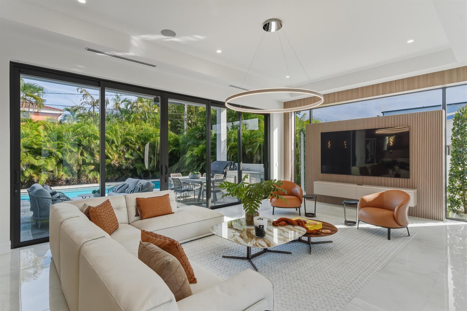 A modern living room features a white sectional, leather chairs, and sliding doors to a pool — 1050 NE 3rd Avenue, Boca Raton FL 33432, BOCA RATON, FL