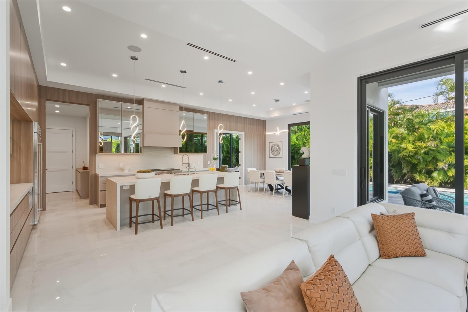A modern kitchen and living area feature white cabinetry, a breakfast island, and outdoor views — 1050 NE 3rd Avenue, Boca Raton FL 33432, BOCA RATON, FL