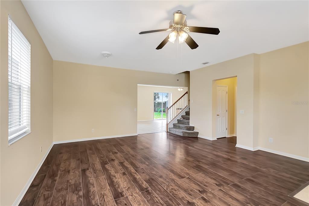 A living room with wood-look tile flooring, a ceiling fan, and stairs leading upstairs — 6767 WATERTON DRIVE, RIVERVIEW, FL