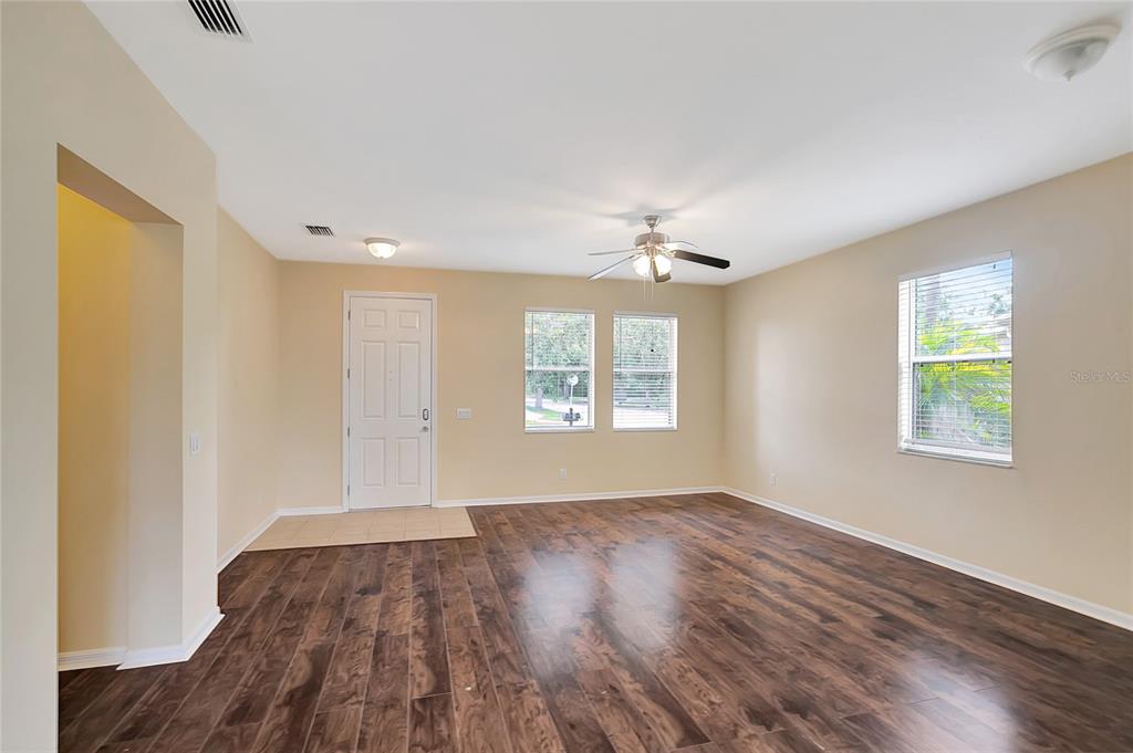 An empty living room features wood-look flooring, beige walls, a ceiling fan, and a front door — 6767 WATERTON DRIVE, RIVERVIEW, FL