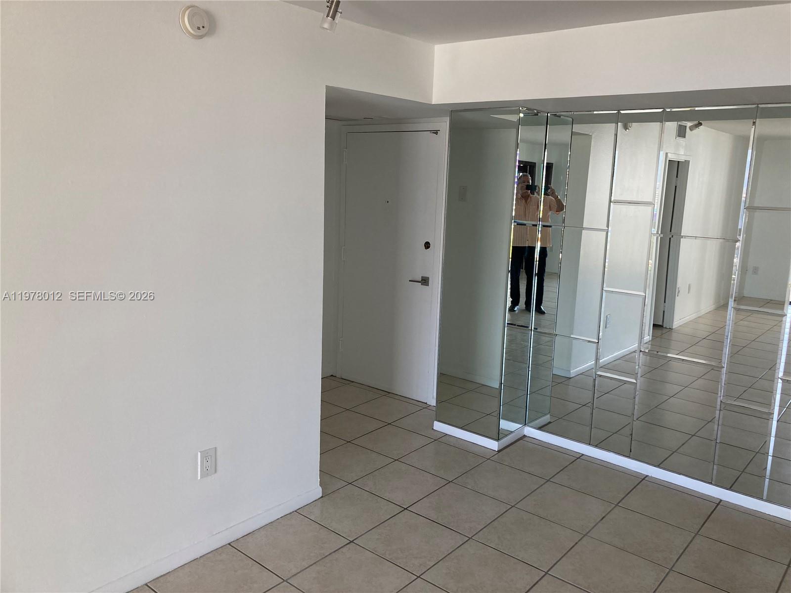 A room with tiled flooring features a white door and a large mirrored wall — 2333 Brickell Ave # 1115, Miami FL 33129, MIAMI, FL