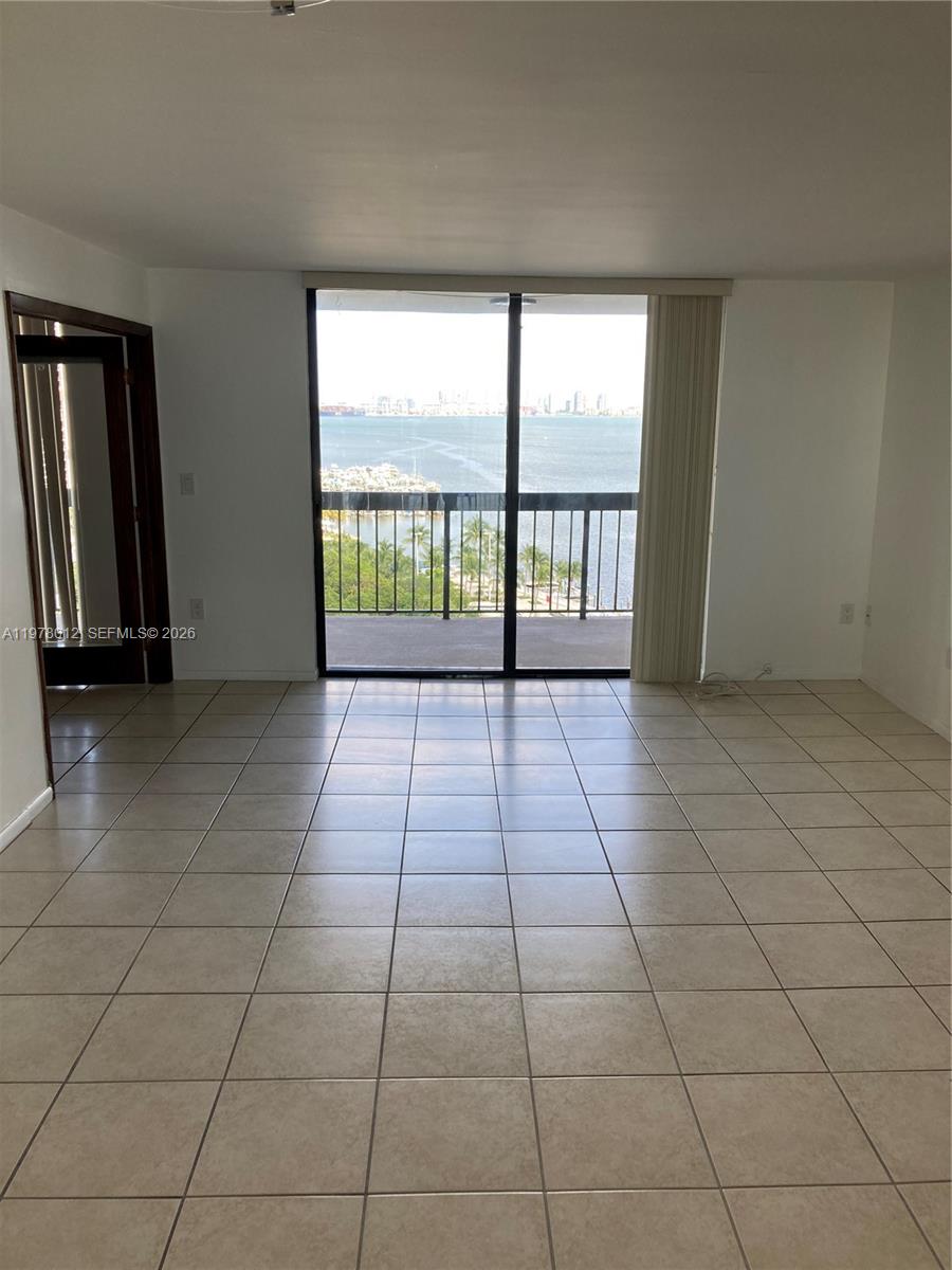An empty room with beige tile flooring features a sliding glass door overlooking the water — 2333 Brickell Ave # 1115, Miami FL 33129, MIAMI, FL