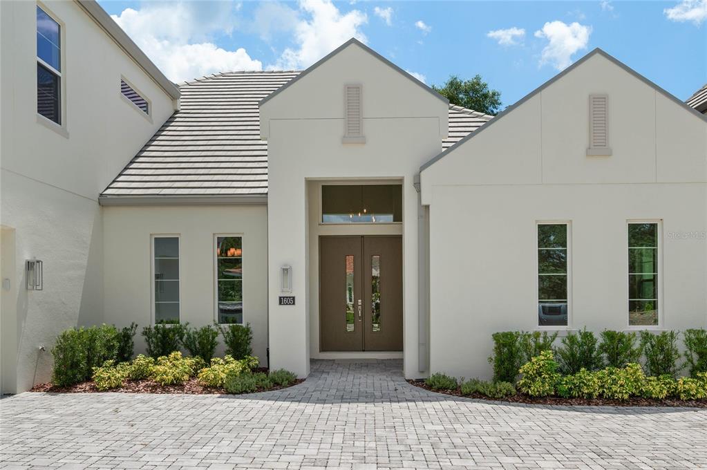 A modern house exterior features a paved driveway, double front doors, and light-colored stucco walls — 1605 MANOR WOODS WAY, SANFORD, FL