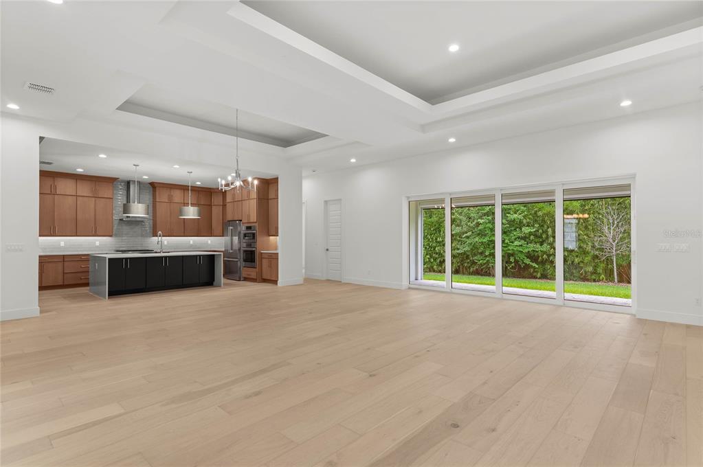 An open-concept kitchen and living area features light wood floors, white walls, and sliding doors — 1605 MANOR WOODS WAY, SANFORD, FL
