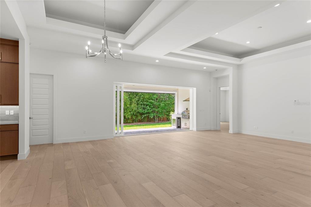 A spacious living room with light wood floors, a tray ceiling, and sliding glass doors — 1605 MANOR WOODS WAY, SANFORD, FL