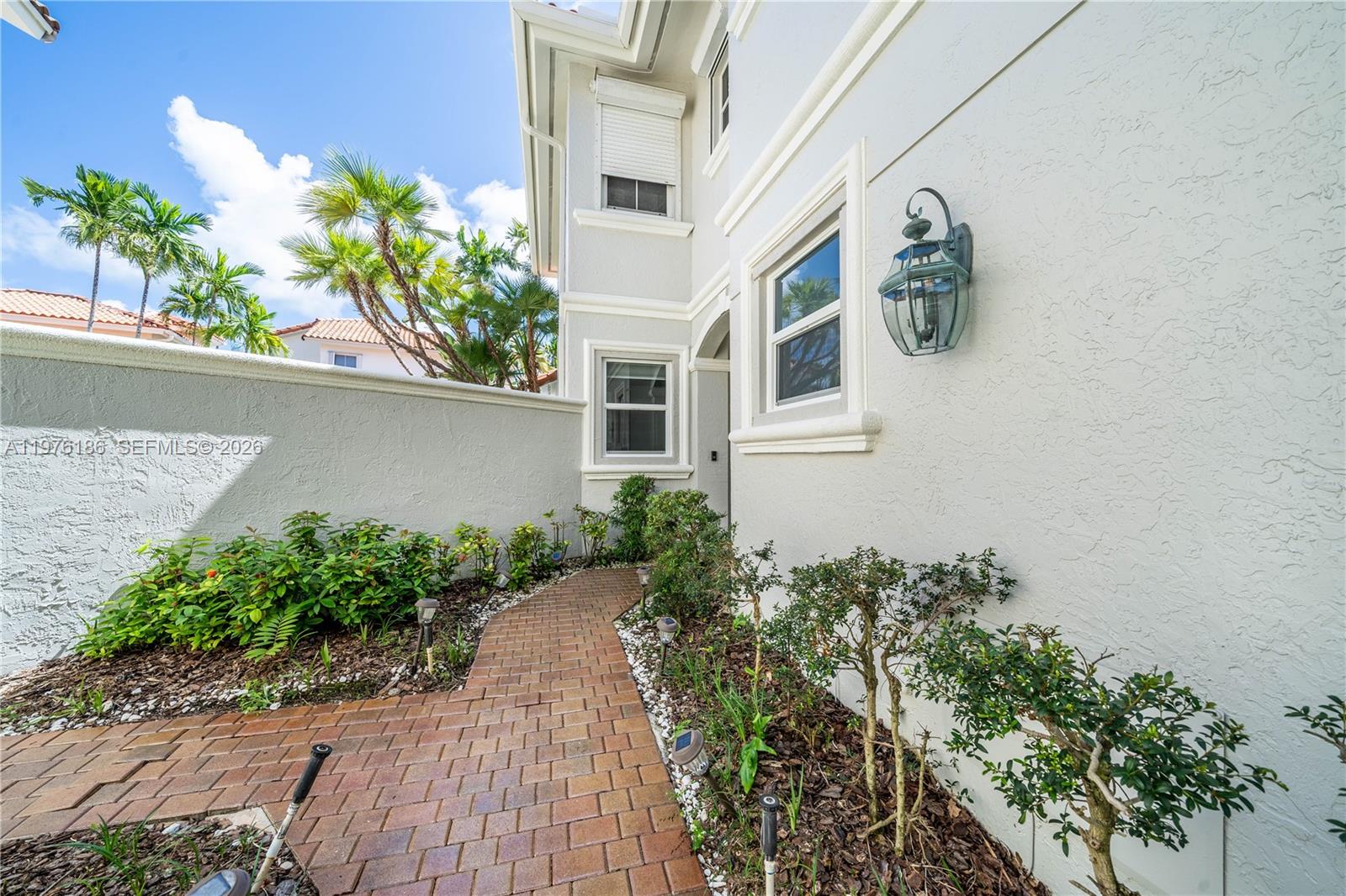 A brick walkway leads to the entrance of a light-colored home with landscaping — 1547 Mariner Way, Hollywood FL 33019, HOLLYWOOD, FL