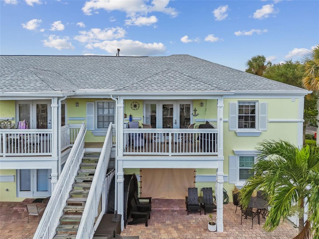 An exterior view of a two-story yellow house with a wooden staircase and patio — 5116 BEACH DRIVE SE UNIT D, ST PETERSBURG, FL