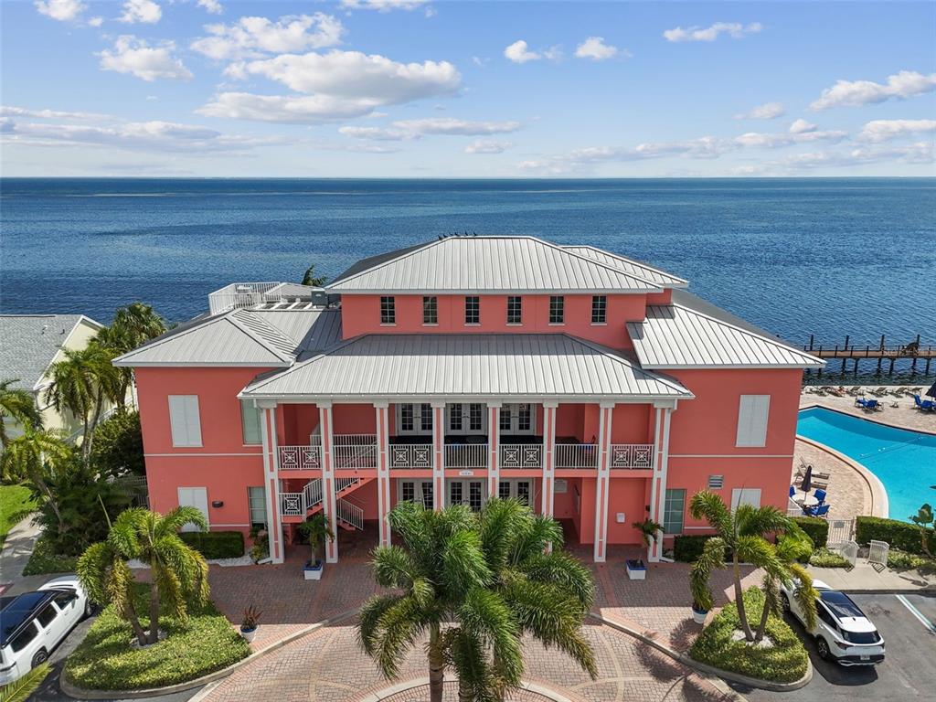 An aerial view of a three-story pink building with a metal roof near the ocean — 5116 BEACH DRIVE SE UNIT D, ST PETERSBURG, FL