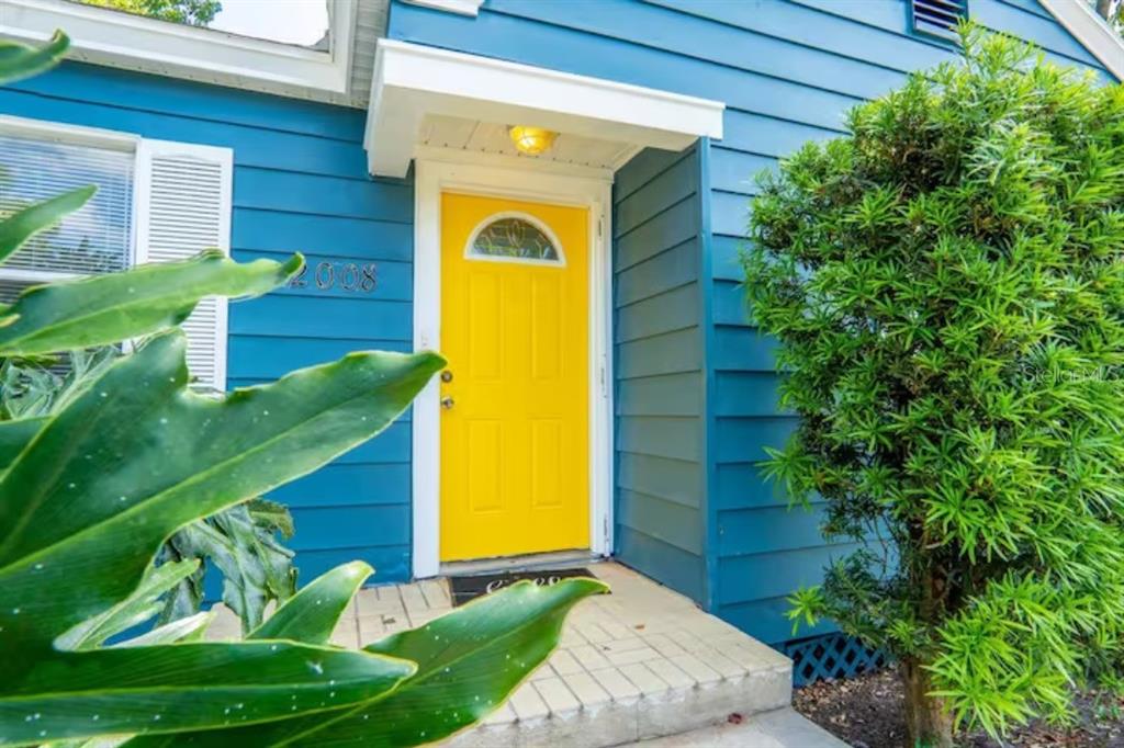 A bright yellow front door is centered on the blue-sided exterior of a house — 2008 PAGE AVENUE, ORLANDO, FL