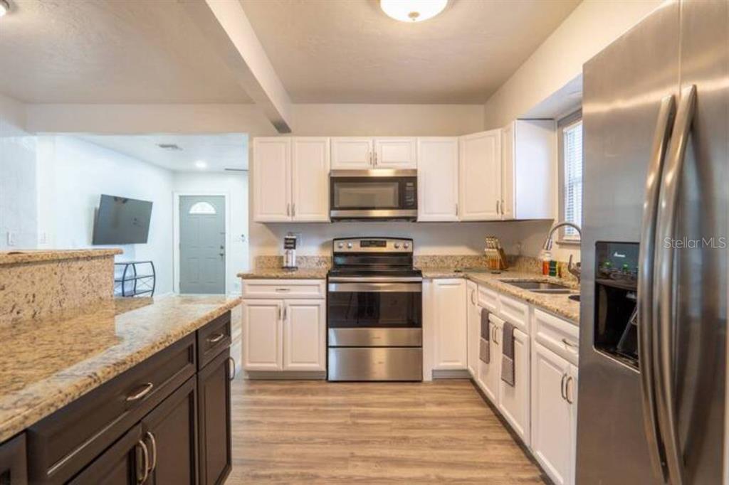 A kitchen features white cabinets, stainless steel appliances, granite countertops, and wood-look flooring — 2008 PAGE AVENUE, ORLANDO, FL