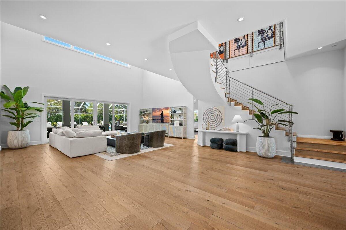 A spacious living room features light wood floors, a curved staircase, and floor-to-ceiling windows — 6209 Homeland Road, Lake Worth FL 33449, LAKE WORTH, FL
