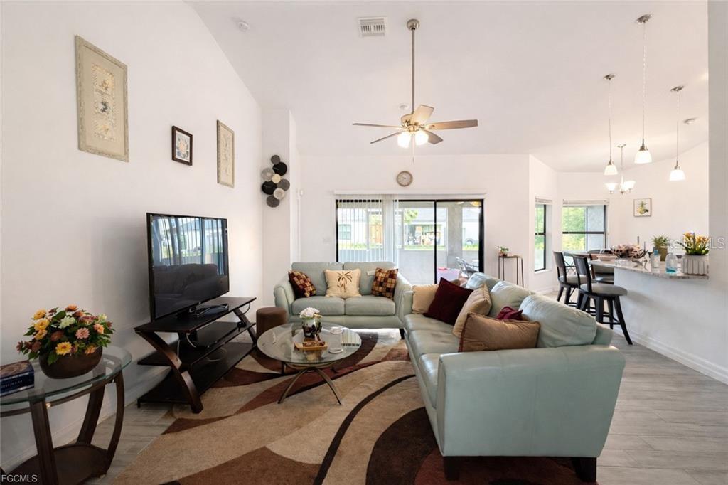 A living room with light blue sofas, a patterned rug, and an open kitchen area — 2917 12TH STREET SW, LEHIGH ACRES, FL