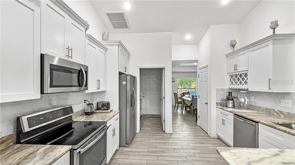 A modern kitchen features white cabinets, stainless steel appliances, and light-colored stone countertops — 2917 12TH STREET SW, LEHIGH ACRES, FL