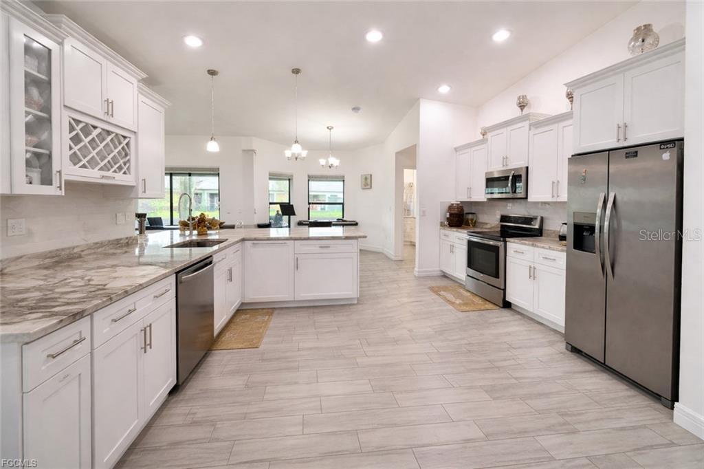 A bright kitchen features white cabinetry, stainless steel appliances, and light-colored wood-look tile flooring — 2917 12TH STREET SW, LEHIGH ACRES, FL