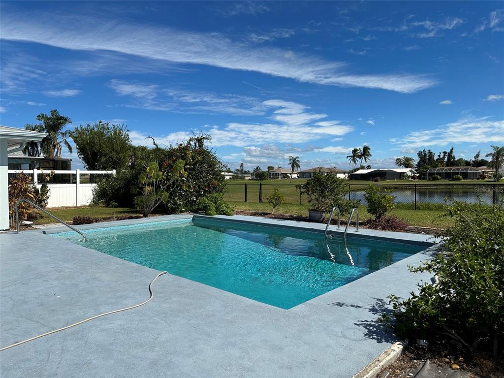 A rectangular swimming pool sits on a concrete patio overlooking a pond and distant houses — 45 OAKLAND HILLS COURT, ROTONDA WEST, FL
