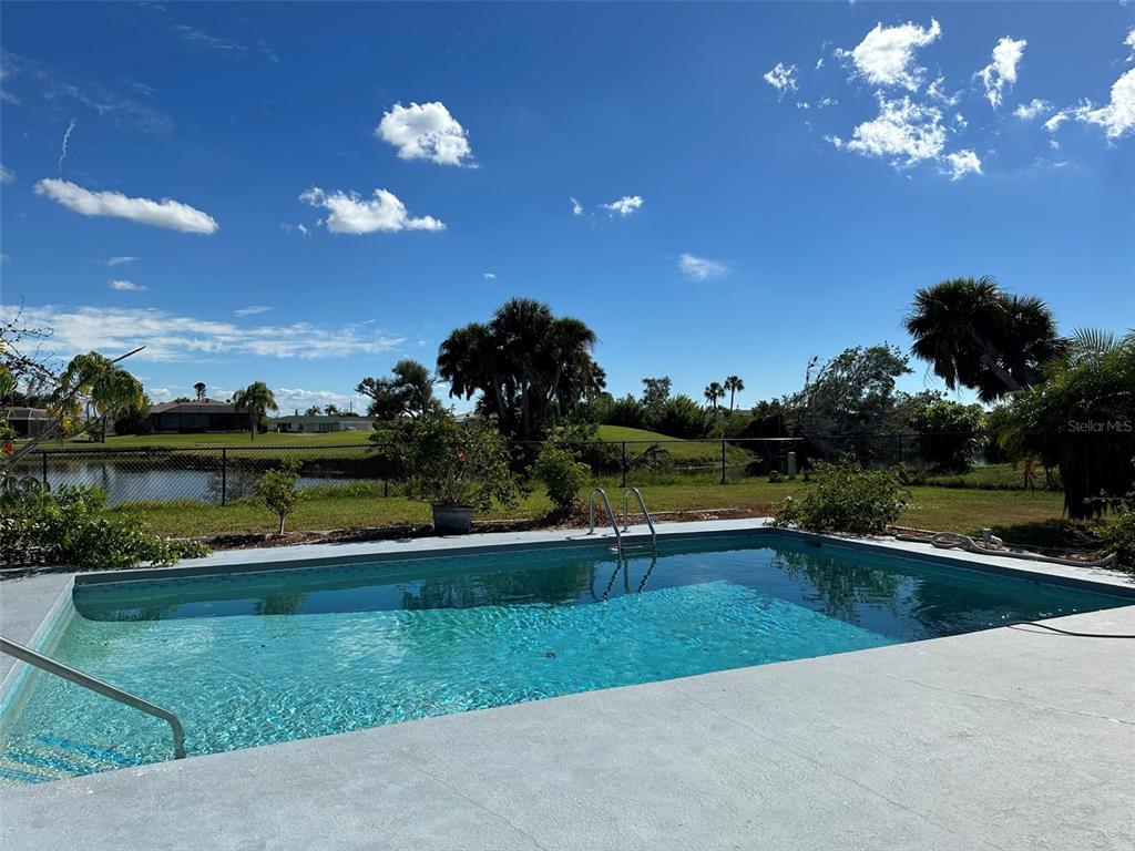 A backyard swimming pool overlooks a pond and grassy landscape under a blue sky — 45 OAKLAND HILLS COURT, ROTONDA WEST, FL