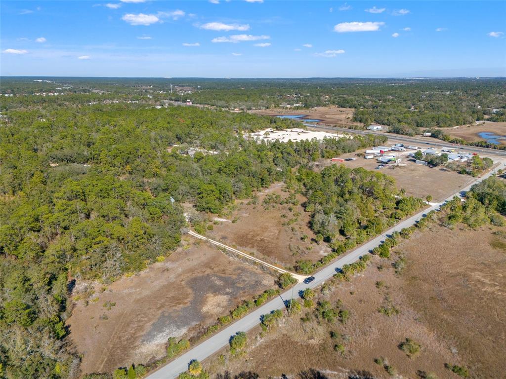 An aerial view shows a paved road bordering a large, partially wooded vacant lot — LONG LAKE AVENUE, WEEKI WACHEE, FL