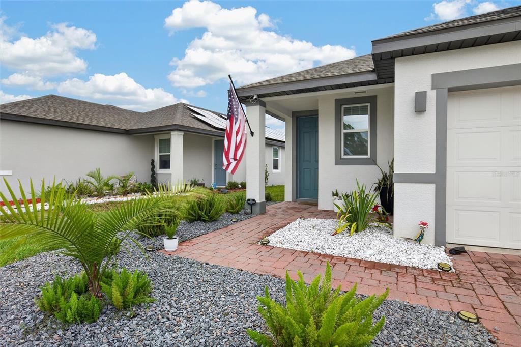 The exterior of a single-story house features a brick walkway, gravel landscaping, and an American flag — 209 LINKS TERRACE BOULEVARD, DAYTONA BEACH, FL