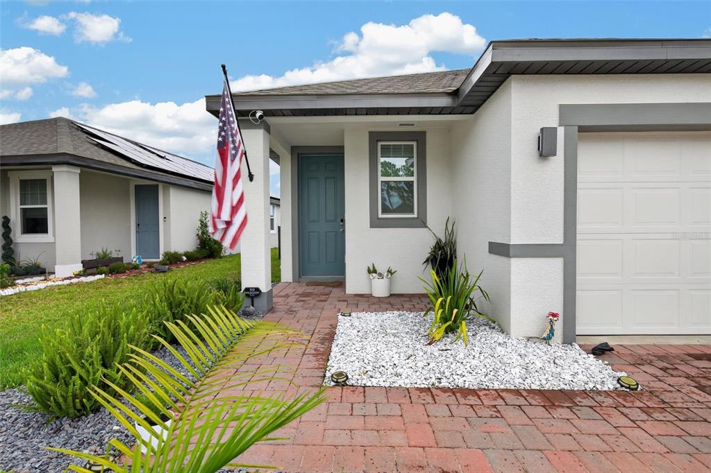 The exterior of a single-story house features a brick walkway, a blue front door, and an American flag — 209 LINKS TERRACE BOULEVARD, DAYTONA BEACH, FL