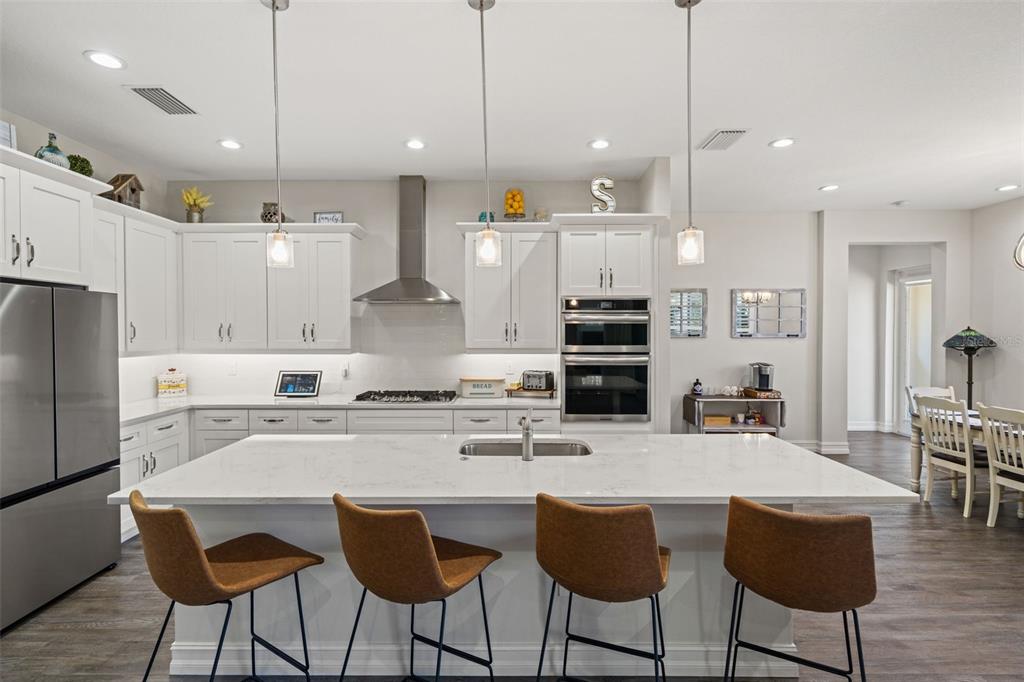A modern kitchen features white cabinetry, a large quartz island with seating, and stainless appliances — 4698 HICKORY OAK DRIVE, BROOKSVILLE, FL