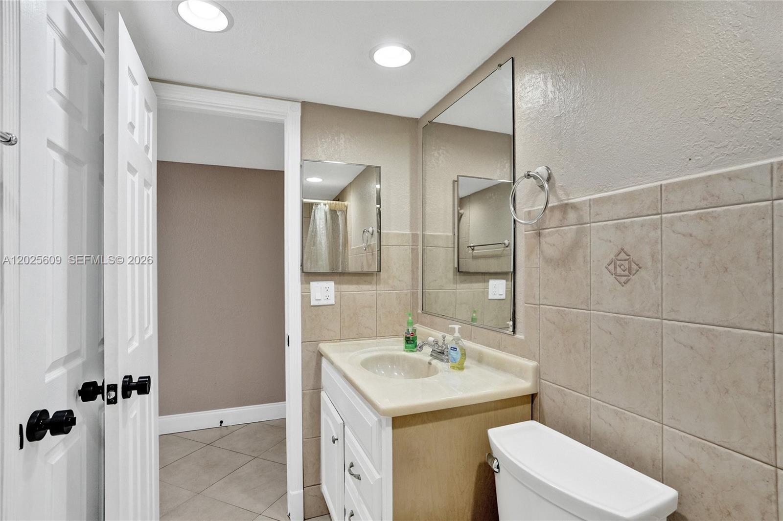 A bathroom features a vanity with a sink, a mirror, and beige wall tiles — 927 NE 199th St # 103, Miami FL 33179, MIAMI, FL
