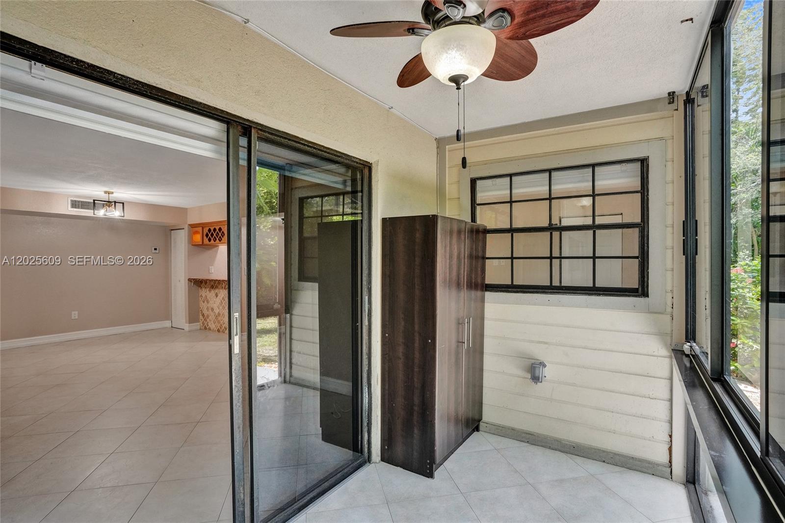 A covered patio features a ceiling fan, a dark cabinet, and sliding glass doors — 927 NE 199th St # 103, Miami FL 33179, MIAMI, FL
