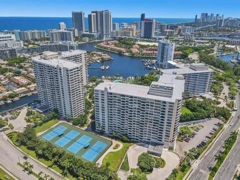 An aerial view shows high-rise apartment buildings, a tennis court, and a waterway in Florida — 2500 Parkview Drive # 814, Hallandale Beach FL 33009, HALLANDALE BEACH, FL