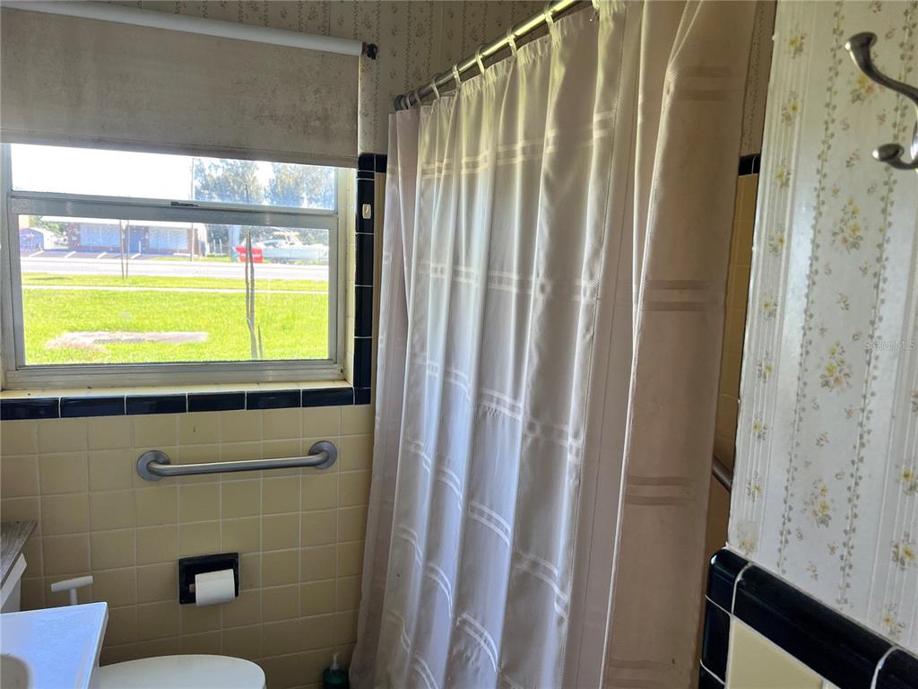 A bathroom features yellow tiled walls, a shower with a curtain, and a window — 104 GRACE AVENUE, COCOA, FL