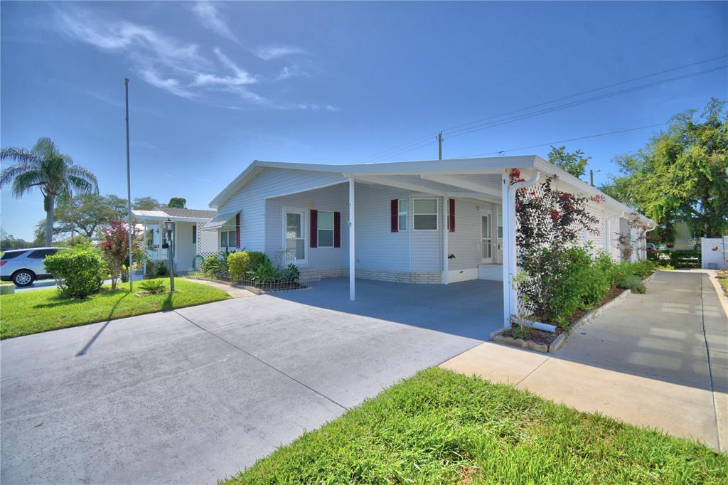 A light blue manufactured home with a concrete driveway, carport, and landscaped front yard — 6086 SOUTHERN OAKS DRIVE, WINTER HAVEN, FL